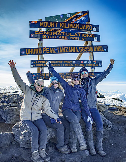 Gezin dat voor het bord bij Uhuru Peak op de top van de Kilimanjaro zit