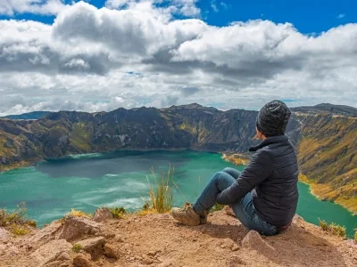 Een vrouw zit aan de rand van het Quilotoa-kratermeer in Ecuador.